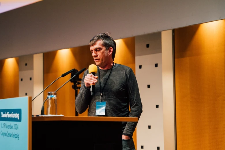 Prof. Hajok referiert hinter einem Pult mit einem Mikrofon in der Hand
