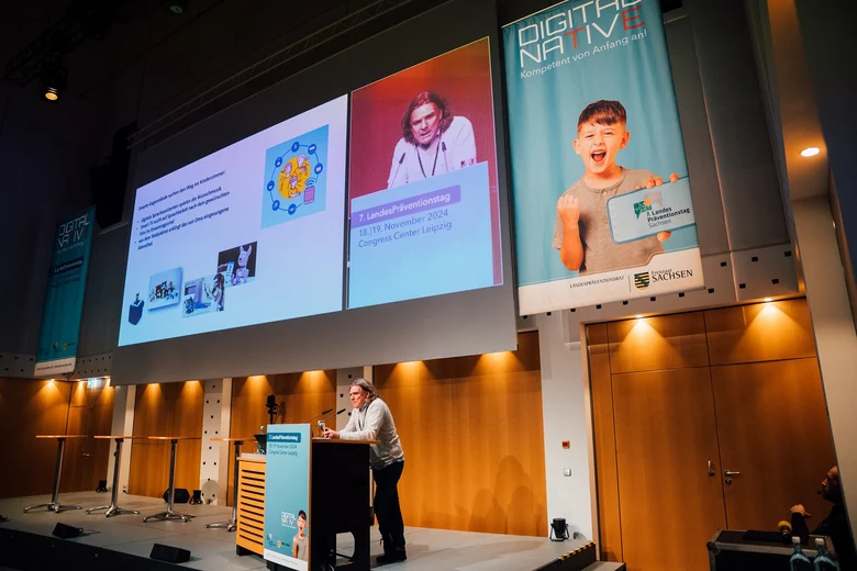 Prof. Dirk Labudde referiert hinter einem Pult vor einer großer Leinwand, vor seiner Präsentation