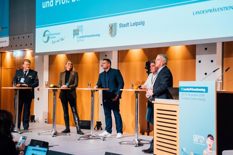 4 Experten auf der Bühne hinter Stehtischen mit einem Mikrofon in der Hand daneben steht der Moderator vorn im Bild das Rednerpult mit dem LPT7 Banner